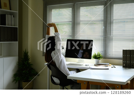 Rear view of relaxed woman stretching at her workstation, enjoying a mindful moment during work 128189260