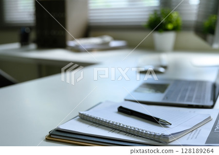 Close up of an office desk with laptop, spiral notebook, pen, and financial document 128189264