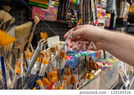 Customer's hand selects a professional paint brush from a large store display of colorful art supplies, symbolizing artistic passion and hobby shopping 128189326