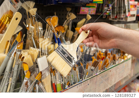 Person hand selecting a wide flat paintbrush from a diverse retail display of various art supplies, highlighting creativity and shopping for new tools 128189327