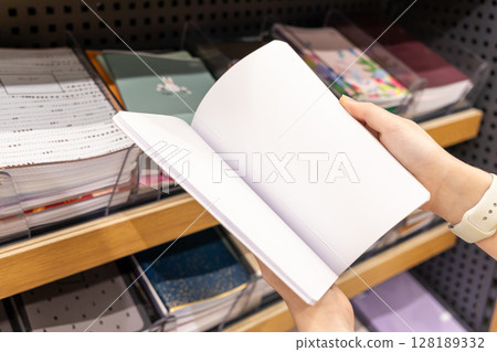 A person's hand holds an open blank white notebook, ready for new concepts, creative expression, or educational studies in a retail environment A person's hand holds an open blank white notebook, ready for new concepts, creative expression, or educational studies in a retail environment 128189332