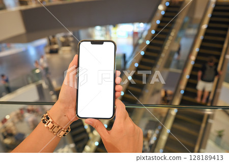 Close up of woman holding a smartphone with blank white screen in a modern shopping mall 128189413