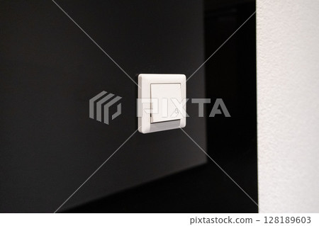Modern white doorbell button featuring a bell icon on a dark wal 128189603