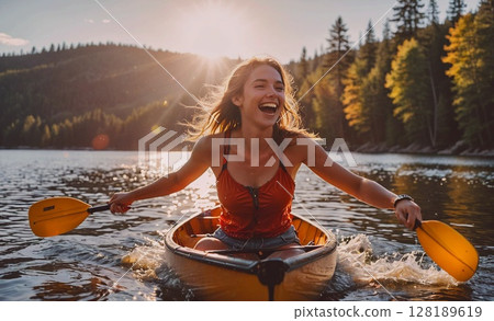 Woman in a red top is paddling a canoe on a lake. She is smiling and enjoying the experience 128189619