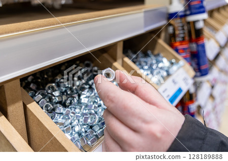 selection of a metal nut from a wooden box in a hardware store, close-up of fastening materials for construction and repair 128189888