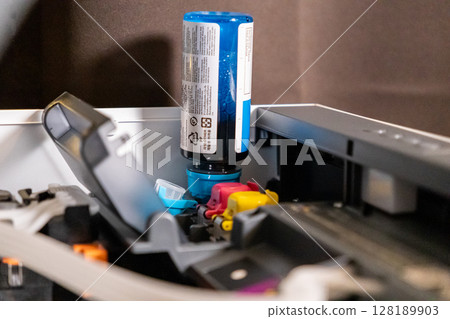 refilling printer ink with blue cartridge bottle in open printer compartment during maintenance process 128189903