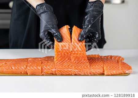 fresh salmon fillet slices being prepared by a chef in black gloves on a white surface fresh salmon fillet slices being prepared by a chef in black gloves on a white surface 128189918