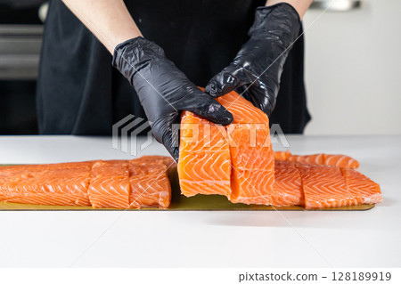 chef preparing fresh salmon fillet slices on white table with black gloves in kitchen setting chef preparing fresh salmon fillet slices on white table with black gloves in kitchen setting 128189919