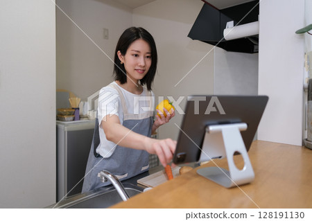 A woman cooking in the kitchen while looking at a tablet 128191130