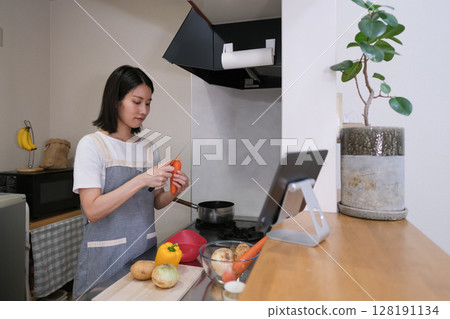 一位女士在廚房做飯,同時看著平板電腦 一位女士在廚房做飯,同時看著平板電腦 128191134