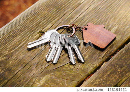 Keys on vintage weathered table. Wooden house shaped keychain. Close up 128191351