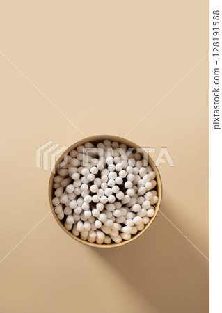 Wooden ecological cotton swab in paper container on beige background. Zero waste, sustainable resources. Close up. Vertical format. Wooden ecological cotton swab in paper container on beige background. Zero waste, sustainable resources. Close up. Vertical format. 128191588