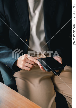 Close-up of a person in business attire using a smartphone, highlighting modern communication and productivity. 128191762