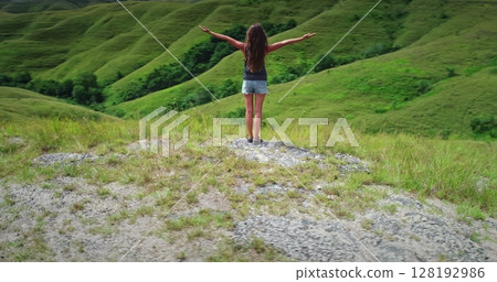 Young woman standing on a hill with open arms, embracing the beauty of nature in Sumba Island, Indonesia, a popular tourist destination known for its unique landscapes and rich culture Young woman standing on a hill with open arms, embracing the beauty of nature in Sumba Island, Indonesia, a popular tourist destination known for its unique landscapes and rich culture 128192986