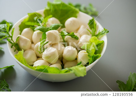 mini mozzarella in white bowl with greens on grey background. Top view 128193556