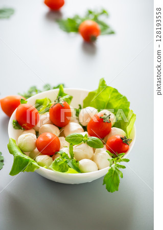 White bowl with mini mozzarella and greens on a gray background 128193558