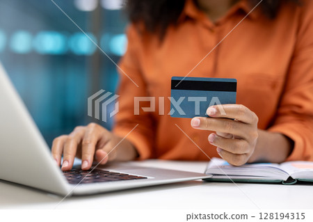 A woman is holding a credit card while typing on a laptop, seemingly making an online purchase or managing her finances 128194315