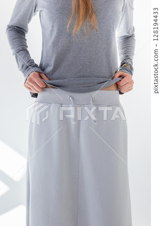 Beautiful woman in gray skirt and T-shirt on white background. Fashionable female style. Studio photography. Vertical photo. High quality photo 128194433