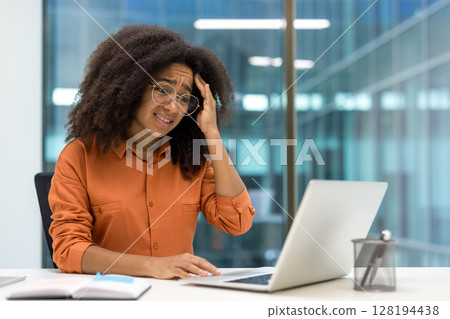 Upset frustrated woman working with laptop inside office. Businesswoman unsatisfied reading online email notification message from laptop. Upset frustrated woman working with laptop inside office. Businesswoman unsatisfied reading online email notification message from laptop. 128194438