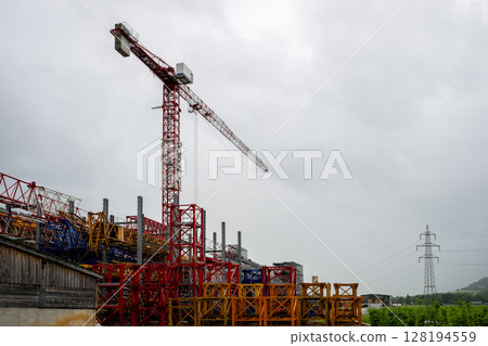 Tall red tower crane and colorful metal structures at construction equipment yard 128194559