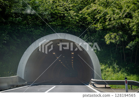 Asphalt road leading into tunnel entrance surrounded by green forest 128194565
