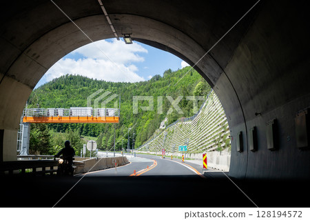 Asphalt road leading out of tunnel to scenic green landscape in summer 128194572