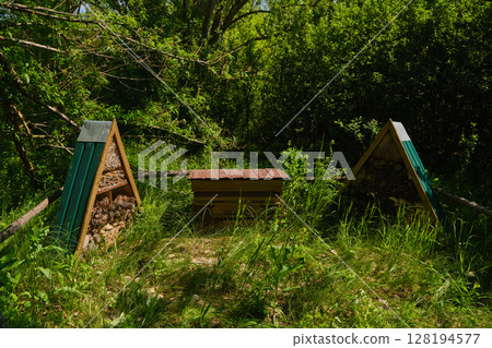 A rustic, triangular insect hotel filled with natural materials sits nestled in tall green grass A rustic, triangular insect hotel filled with natural materials sits nestled in tall green grass 128194577