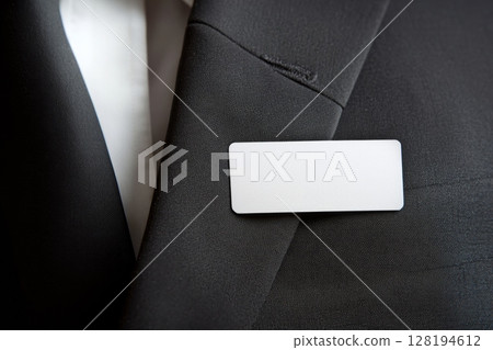 Close-up view of a blank white name badge pinned to a dark business suit jacket 128194612