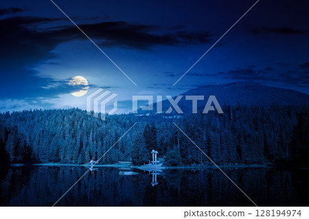 scenic landscape with lake among coniferous forest at night. tranquil reflection of primeval woodland in mountains in full moon light scenic landscape with lake among coniferous forest at night. tranquil reflection of primeval woodland in mountains in full moon light 128194974