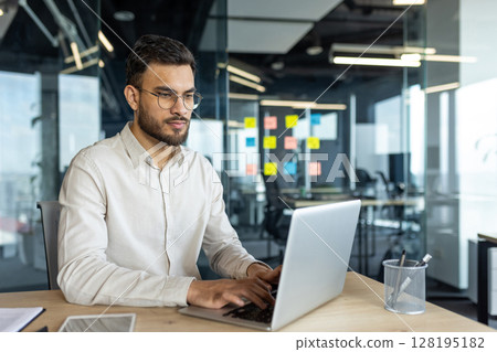 Latin American businessman focused on his work while using a laptop in a bright, professional office environment, embodying dedication, focus, and professionalism in a corporate setting. Latin American businessman focused on his work while using a laptop in a bright, professional office environment, embodying dedication, focus, and professionalism in a corporate setting. 128195182