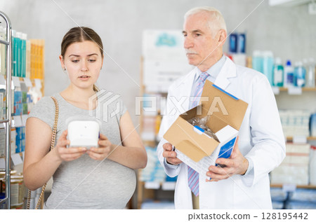 Young pregnant client choosing tonometer while pharmacist offering in drugstore 128195442