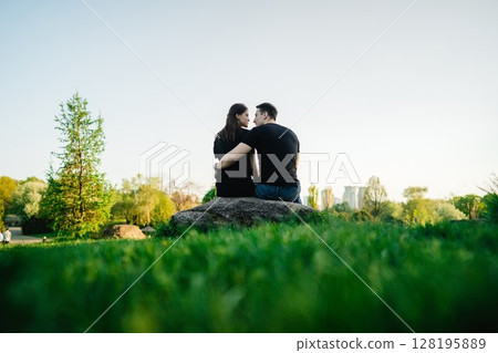 Couple enjoying a quiet moment on a rock in a serene park at sunset 128195889