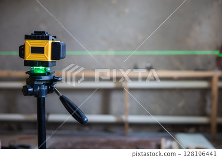 A laser level mounted on a tripod projects a green line onto a construction site. A laser level is essential for precise alignment and measurements in construction projects. 128196441