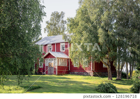 Traditional red wooden house surrounded by summer greenery in rural Finland 128196718