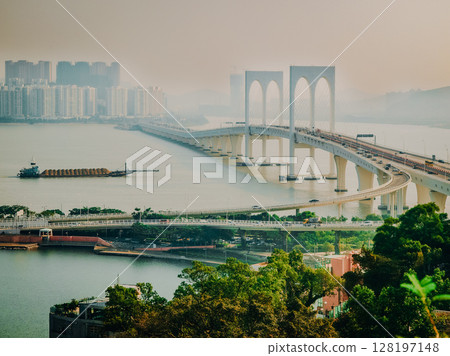 Macau Bridge Crossing Pearl River Estuary: Elegant White Arches Connecting City Districts Over Calm Waters With High-Rises In The Background On A Hazy Afternoon 128197148