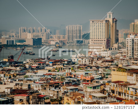 Urban Cityscape Of Macau From Above: Colorful Rooftops Of Historic District Blending Into High-Rise Buildings And Harbor Activity Across The Water On A Hazy Day Urban Cityscape Of Macau From Above: Colorful Rooftops Of Historic District Blending Into High-Rise Buildings And Harbor Activity Across The Water On A Hazy Day 128197157
