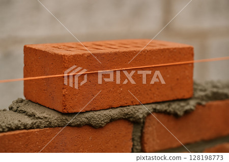 Red brick aligned by masonry string on a bed of mortar during precise bricklaying at a construction site, illustrating building techniques, AI Generative 128198773