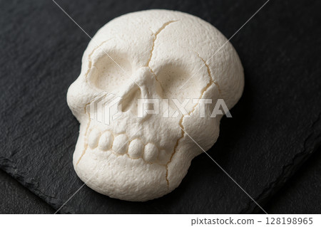 White meringue skull dessert on black slate with detailed cracks and textures, creative halloween themed sweet treat design, AI Generative 128198965