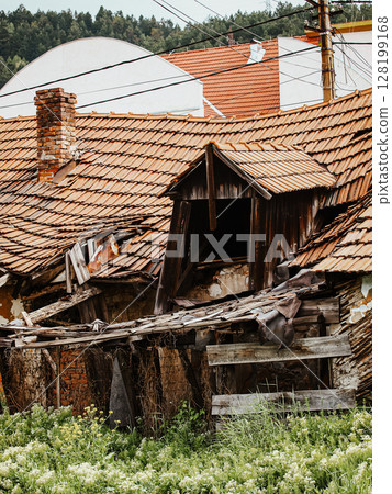 Collapsing Wooden House With A Broken Roof And Crumbling Walls: An Abandoned Rural Structure Overgrown With Greenery And Wildflowers In A Natural Landscape Collapsing Wooden House With A Broken Roof And Crumbling Walls: An Abandoned Rural Structure Overgrown With Greenery And Wildflowers In A Natural Landscape 128199168