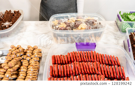 From an overhead perspective, a bakers hands carefully arrange freshly baked gingerbread cookies in neat rows on a marble countertop. The festive assortment, including chocolate-dipped and red-iced 128199242