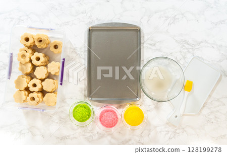 Top-down view of baking tray with plain flower cookies surrounded by decorating tools and ingredients for the Easter Cookie Sandwich with Raspberry Buttercream. Great for baking class visuals. 128199278