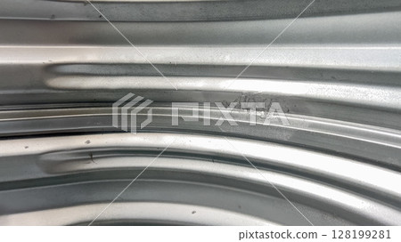 Detailed view of the metallic surface of a basement window well showing natural wear and texture. The lighting emphasizes curved ridges and material imperfections. Detailed view of the metallic surface of a basement window well showing natural wear and texture. The lighting emphasizes curved ridges and material imperfections. 128199281