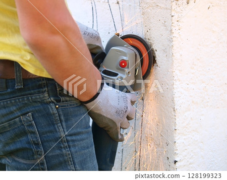 Worker Using an Angle Grinder to Cut Concrete: Sparks Flying as Construction Worker in Gloves and Yellow Shirt Operates Power Tool on Rough Surface Worker Using an Angle Grinder to Cut Concrete: Sparks Flying as Construction Worker in Gloves and Yellow Shirt Operates Power Tool on Rough Surface 128199323