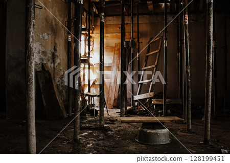 Abandoned Construction Site With Rusty Metal Poles And Wooden Planks: A Dark And Gritty Interior With Scattered Debris And A Broken Ladder In A Decaying Unfinished Building Abandoned Construction Site With Rusty Metal Poles And Wooden Planks: A Dark And Gritty Interior With Scattered Debris And A Broken Ladder In A Decaying Unfinished Building 128199451