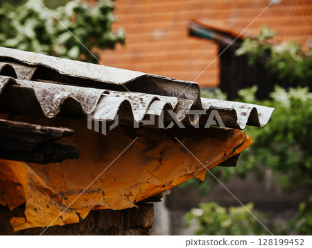 Collapsing Wooden House With A Broken Roof And Crumbling Walls: An Abandoned Rural Structure Overgrown With Greenery And Wildflowers In A Natural Landscape Collapsing Wooden House With A Broken Roof And Crumbling Walls: An Abandoned Rural Structure Overgrown With Greenery And Wildflowers In A Natural Landscape 128199452