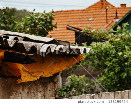 Collapsing Wooden House With A Broken Roof And Crumbling Walls: An Abandoned Rural Structure Overgrown With Greenery And Wildflowers In A Natural Landscape Collapsing Wooden House With A Broken Roof And Crumbling Walls: An Abandoned Rural Structure Overgrown With Greenery And Wildflowers In A Natural Landscape 128199454