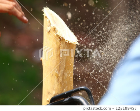 Close-Up Of A Worker Using A Chainsaw To Cut Wood: A Powerful Action Shot Capturing Sawdust Flying As The Blade Slices Through A Log In An Outdoor Setting. Close-Up Of A Worker Using A Chainsaw To Cut Wood: A Powerful Action Shot Capturing Sawdust Flying As The Blade Slices Through A Log In An Outdoor Setting. 128199455