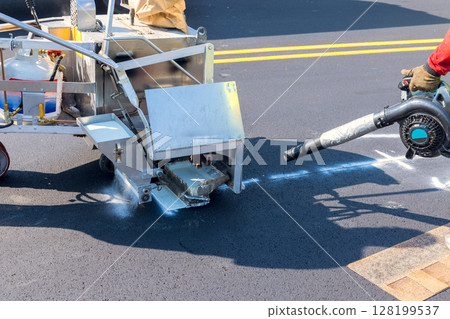 Workers operate road striping machine on newly paved street while ensuring accurate paint application for safety. Workers operate road striping machine on newly paved street while ensuring accurate paint application for safety. 128199537