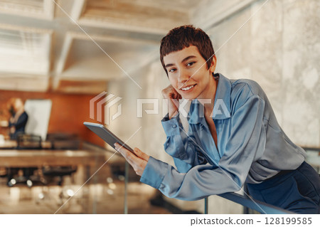 A Stylish and Professional Woman is Engaged with a Tablet in a Contemporary Workspace Setting 128199585