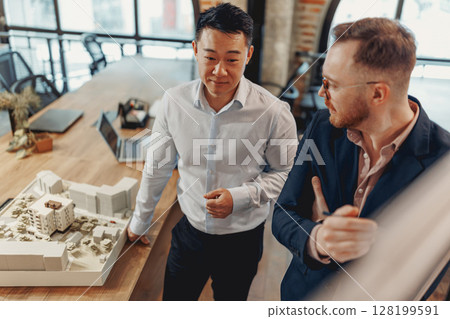 Architects discuss a project model in a modern office, highlighting collaboration and innovation Architects discuss a project model in a modern office, highlighting collaboration and innovation 128199591